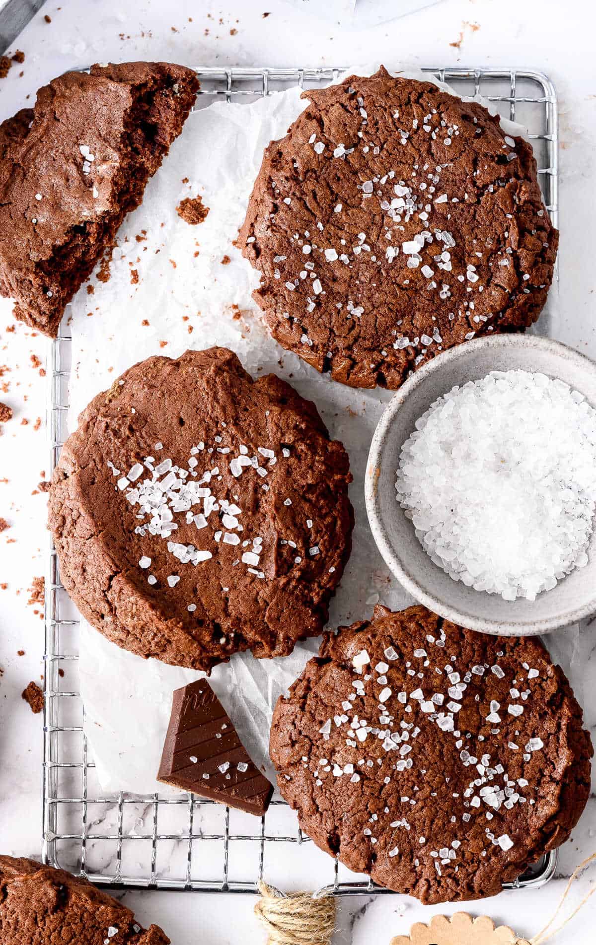 Tres galletas de brownie con un plato de sal marina y trozos de chocolate.