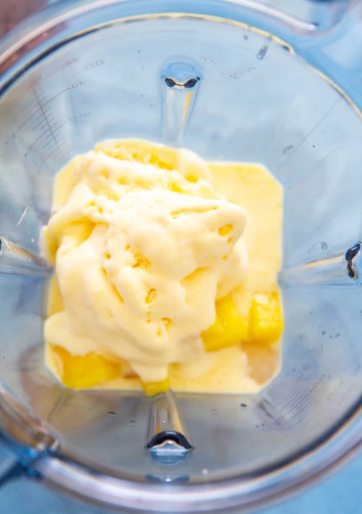 Piña congelada y helado y jugo puesto en una licuadora.