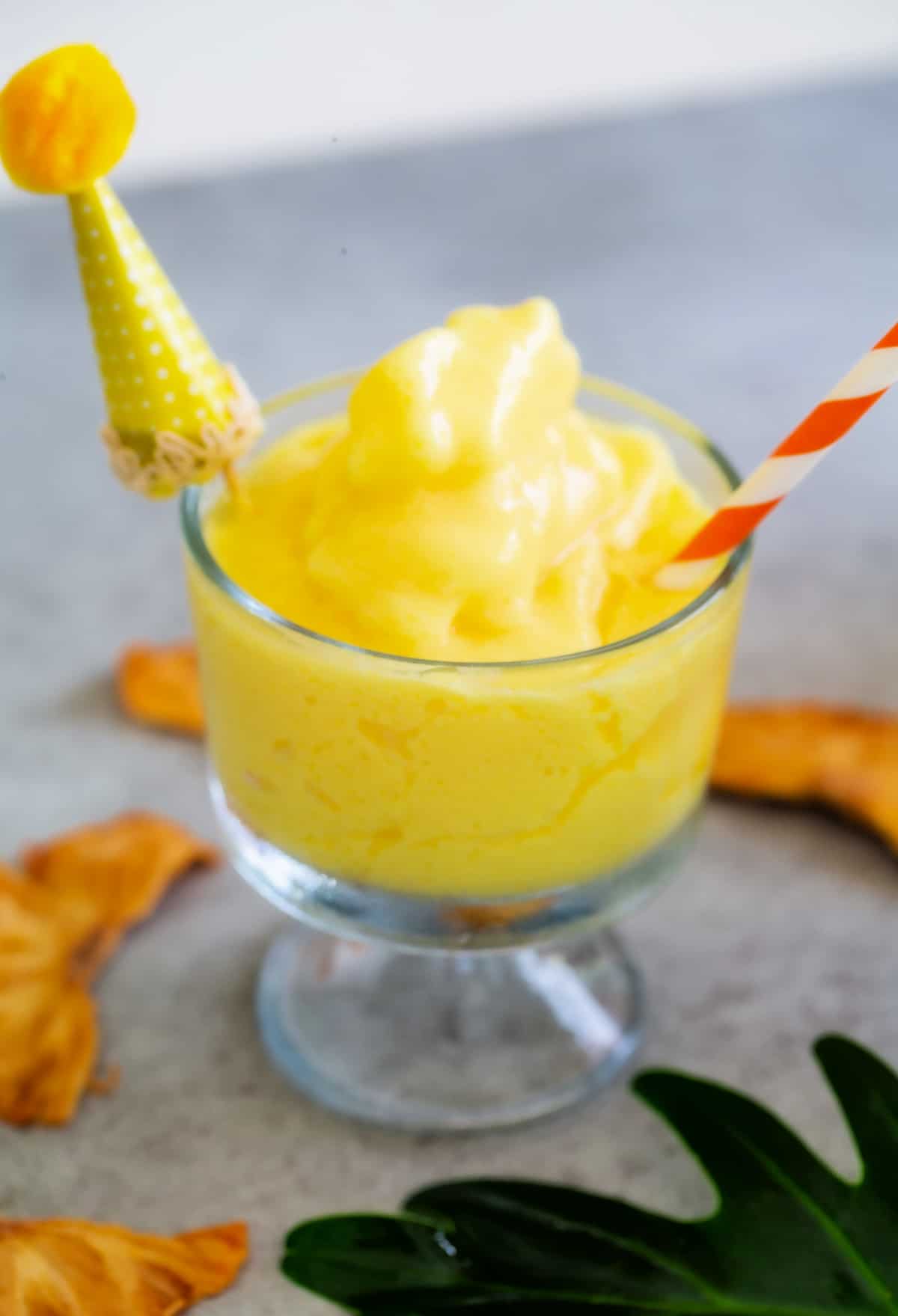 Batidor de manzana de piña casero en un vaso con un sombrero de fiesta decorativo amarillo y una pajita de rayas rojas.