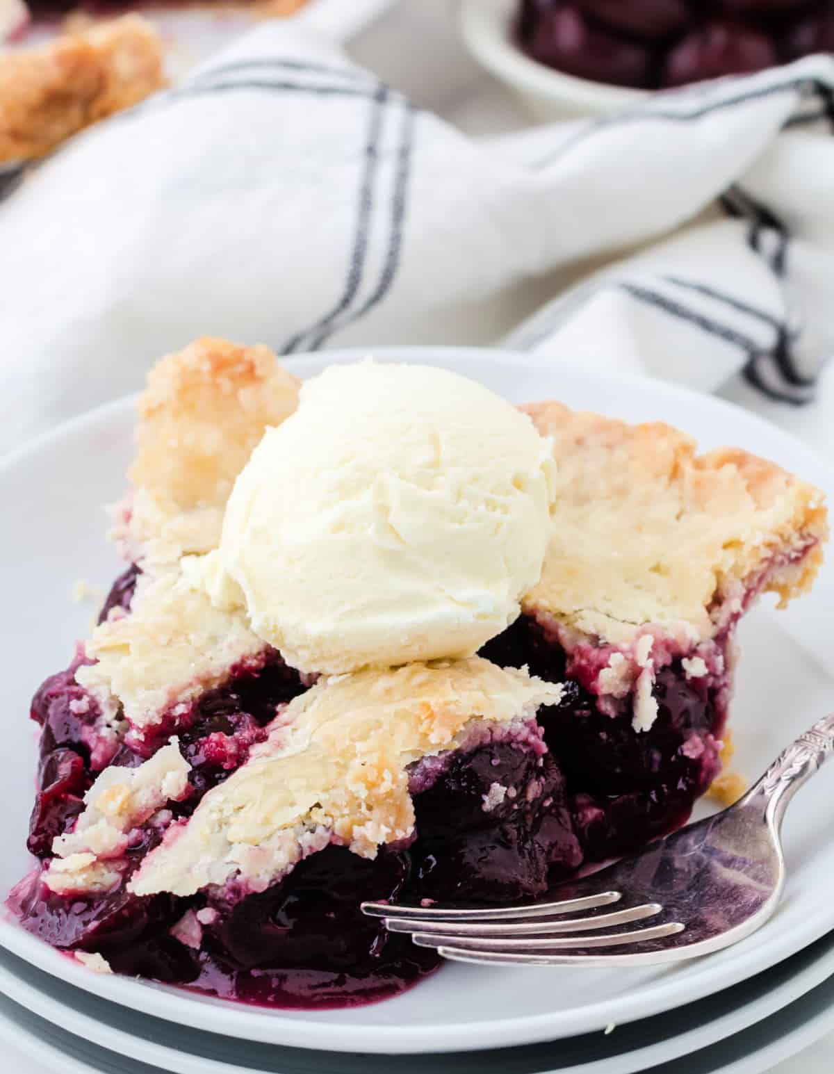 Un trozo de pastel de cereza en un plato blanco con una bola de helado de vainilla.