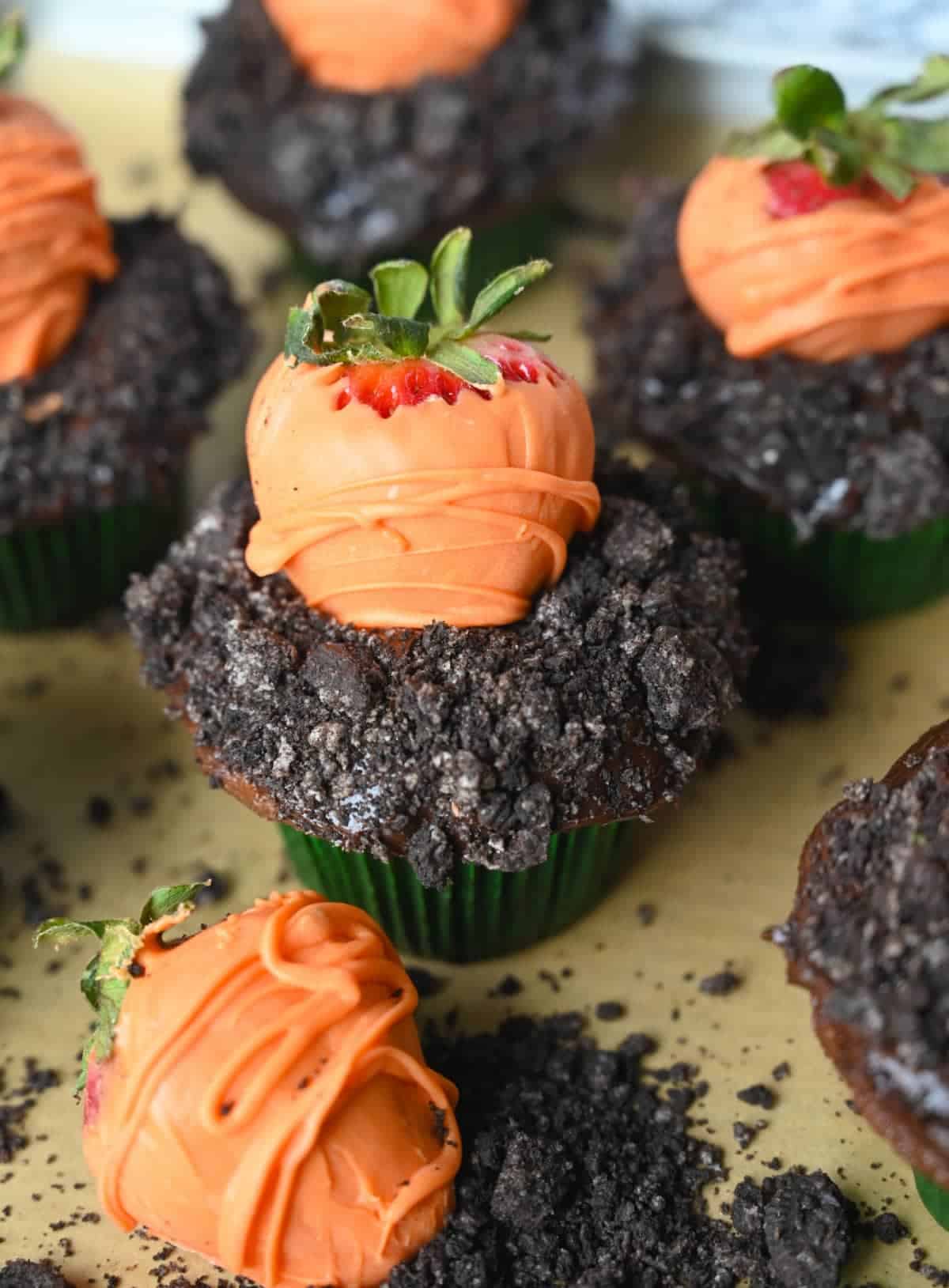 Cinco cupcakes de chocolate con oreo picado encima para que parezca tierra y una fresa cubierta de chocolate encima para que parezca una zanahoria.