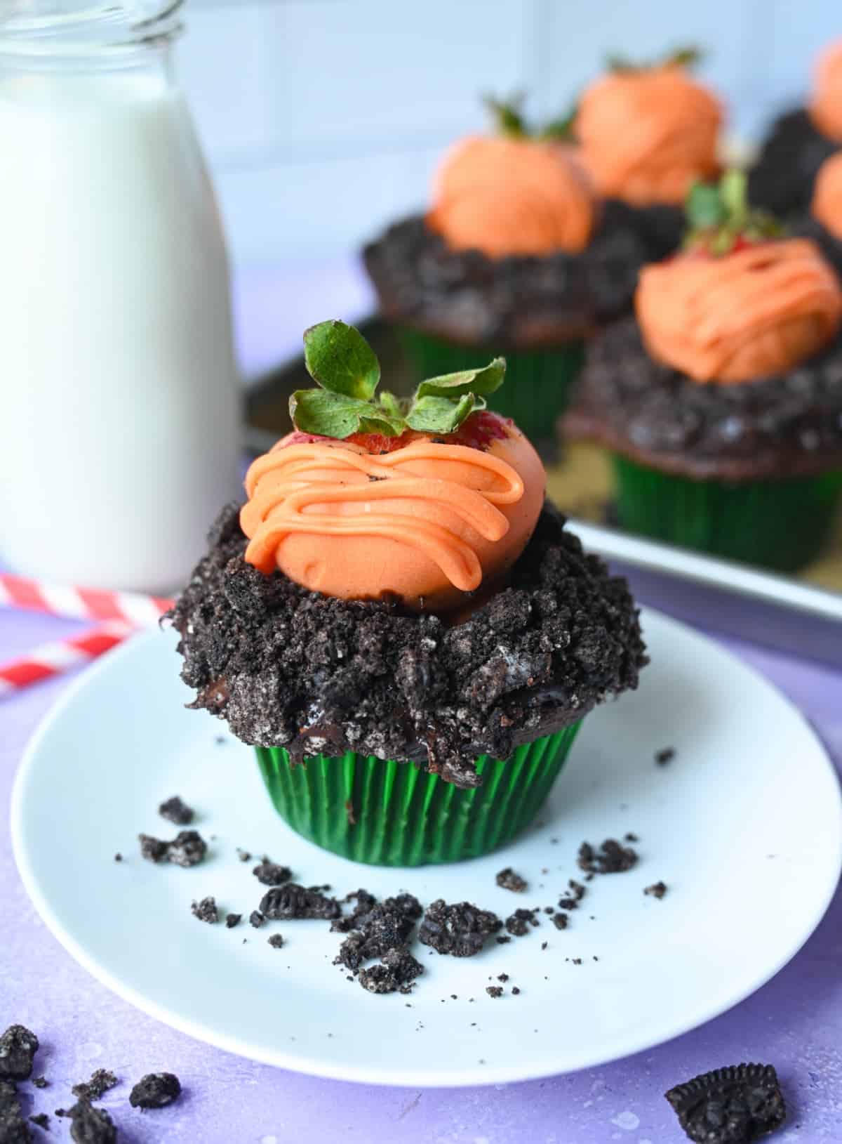 Un cupcake de chocolate con migas de oreo encima y una fresa cubierta de chocolate encima para que parezca una zanahoria.