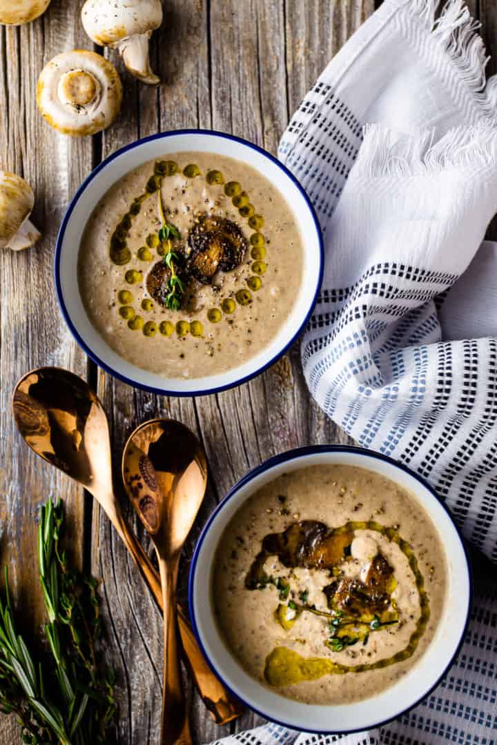 Imagen superior de la receta de sopa de champiñones, preparada y servida en una mesa de madera envejecida con cucharas de oro rosa.