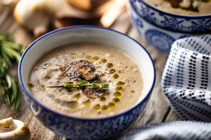 Primer plano de la receta de Crema de Champiñones, preparada y adornada con pimienta negra molida, aceite de trufa y una ramita de tomillo.