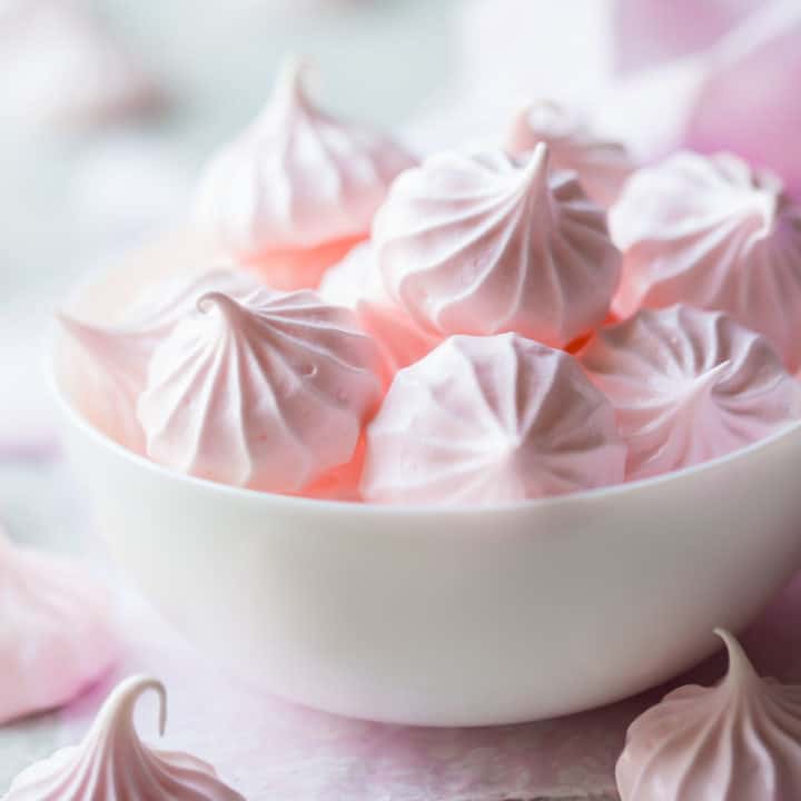 Besos de merengue rosa pálido en un tazón blanco.