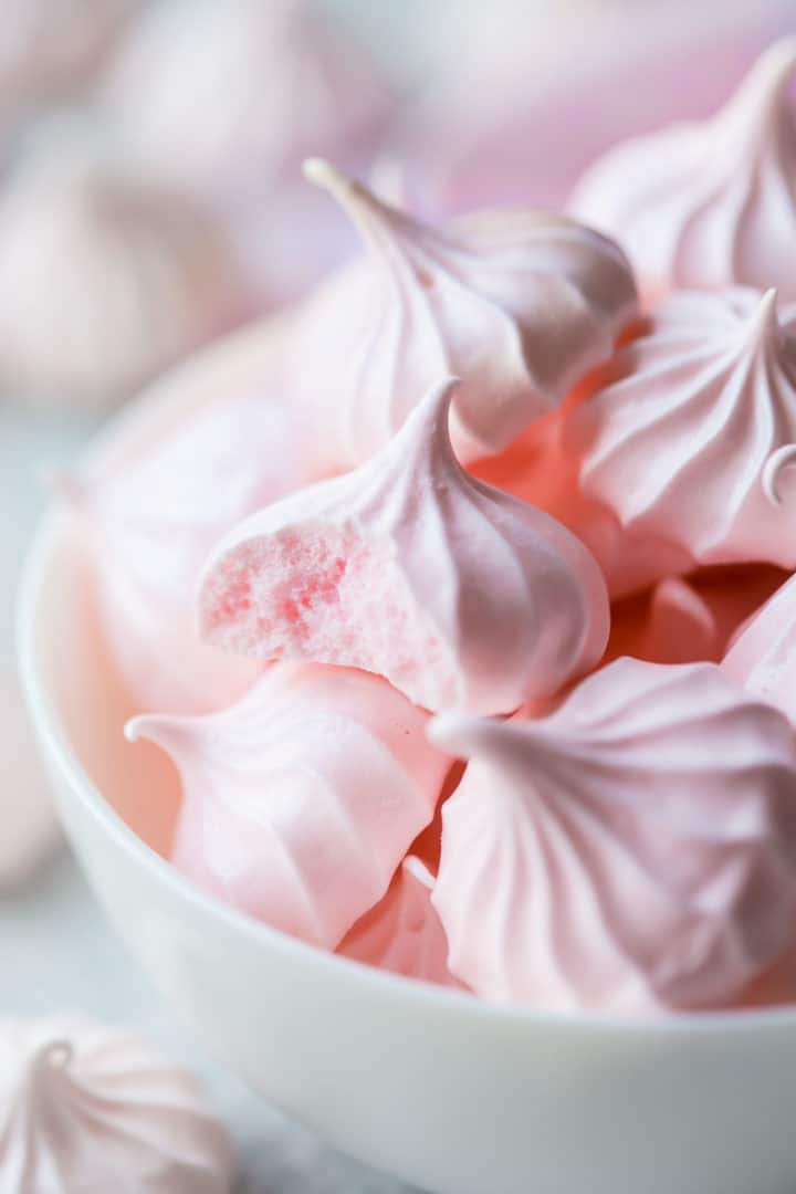 Primer plano de una galleta de merengue horneada con un bocado, que muestra el interior amplio y luminoso.