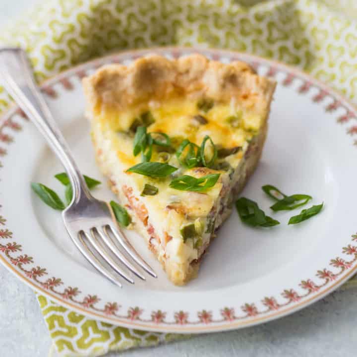 Una rebanada de quiche Lorraine en un plato de porcelana con una servilleta verde estampada.