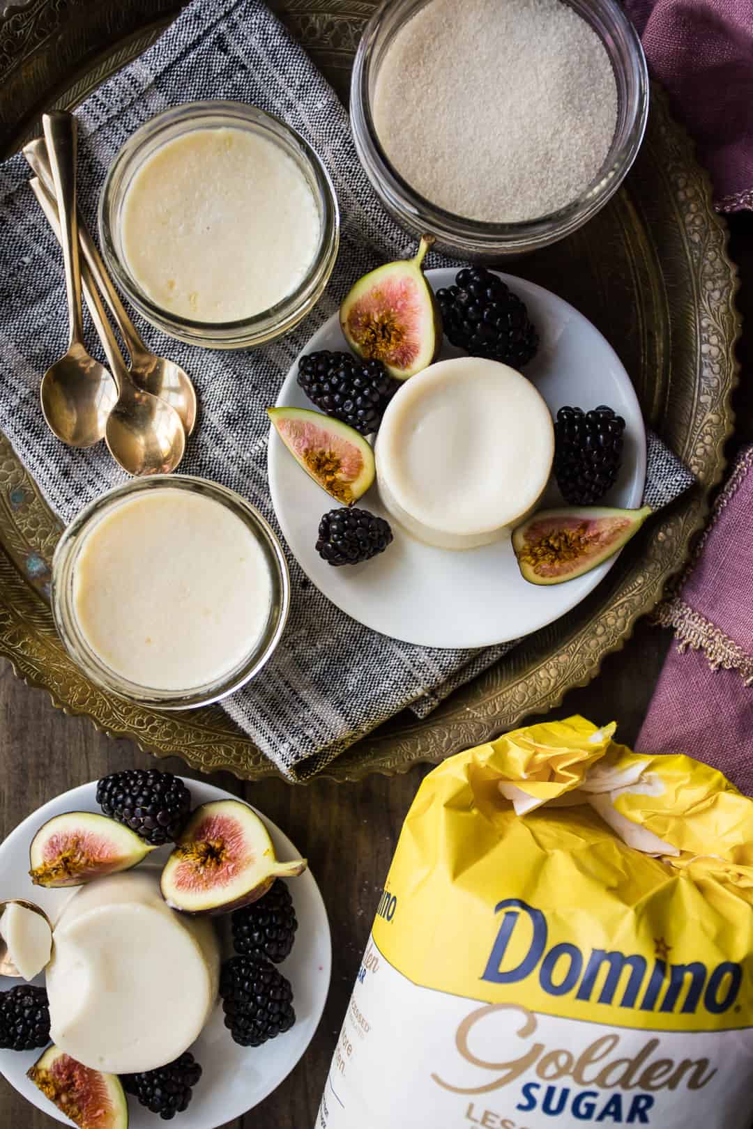 Receta clásica de panna cotta, sobre mesa de madera con azúcar dorada y cucharas de postre doradas.