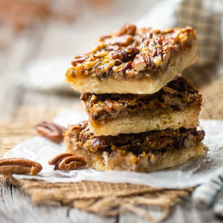 Barras de pastel de nueces apiladas en papel encerado, con nueces enteras en el fondo.