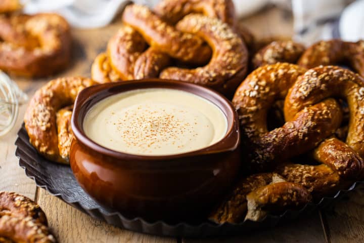 Receta de salsa de queso y cerveza, preparada y servida en un tazón panzón marrón, con suaves pretzels de fondo.