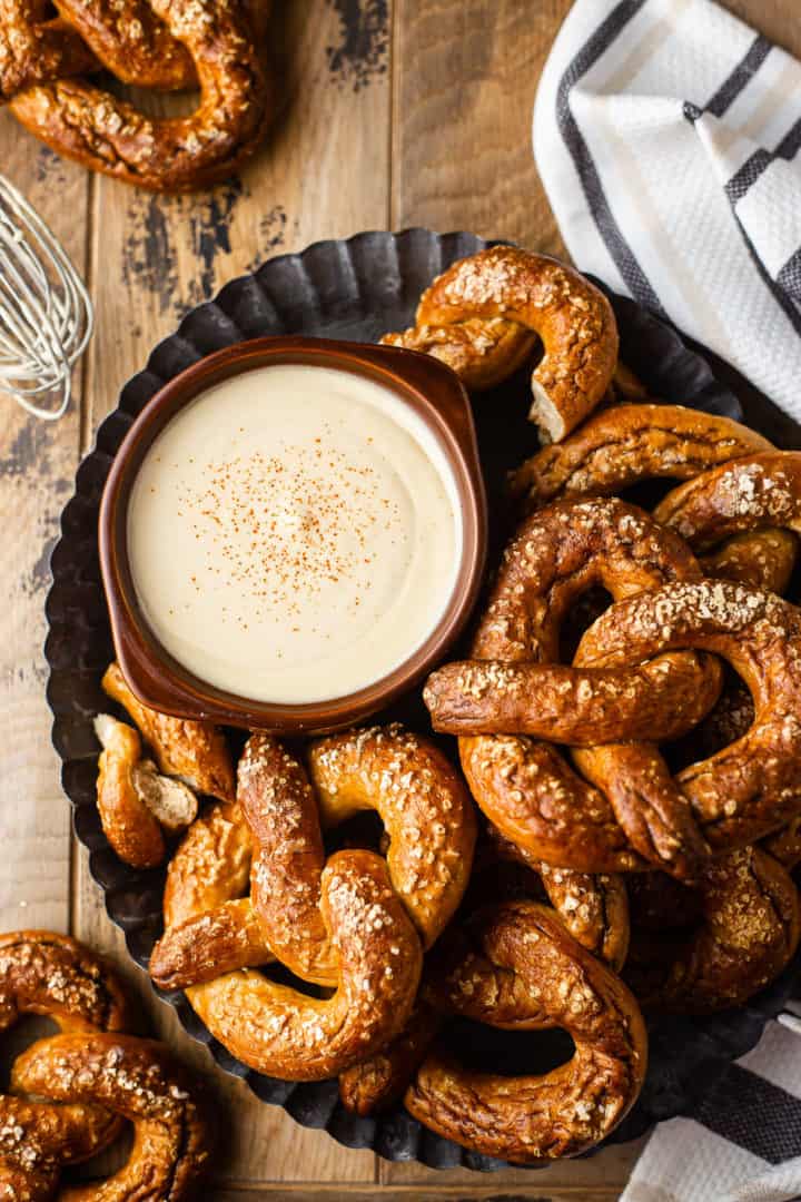 Imagen aérea de la receta de queso a la cerveza, preparada y servida en un tazón marrón y rodeada de pretzels esponjosos.