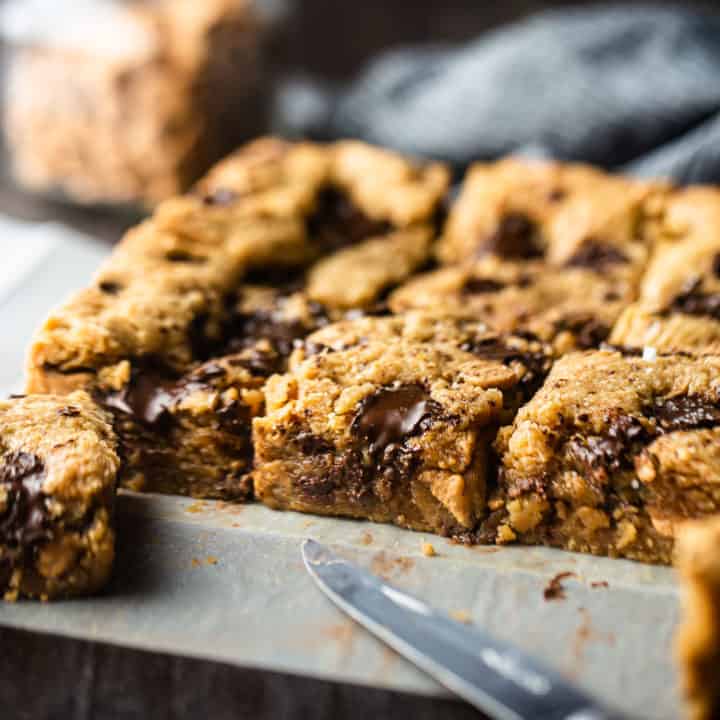 Blondies de mantequilla de maní en una hoja de pergamino cortada en cuadrados.