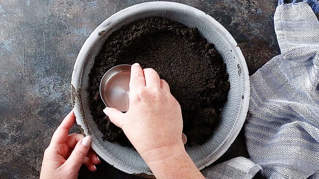 Presione la corteza de Oreo en un molde para pasteles con una taza medidora.