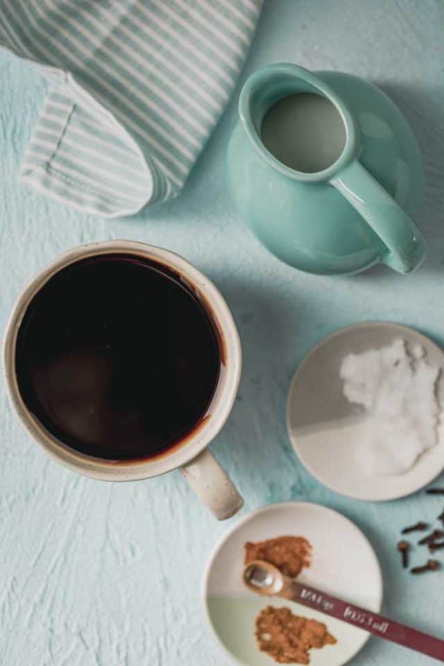 Diseño plano de ingredientes para preparar café con aceite de coco, incluida una taza de café recién hecho, aceite de coco, leche de coco con pimienta de cayena y canela en polvo, que son opcionales.