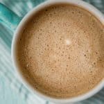 Primer plano de café mezclado con aceite de coco, que muestra una taza espumosa y cremosa con una servilleta azul debajo