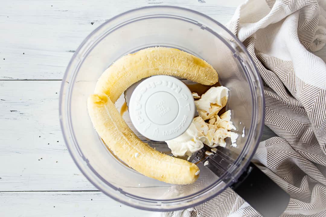 Plátanos, crema agria y vainilla en el recipiente de un procesador de alimentos.