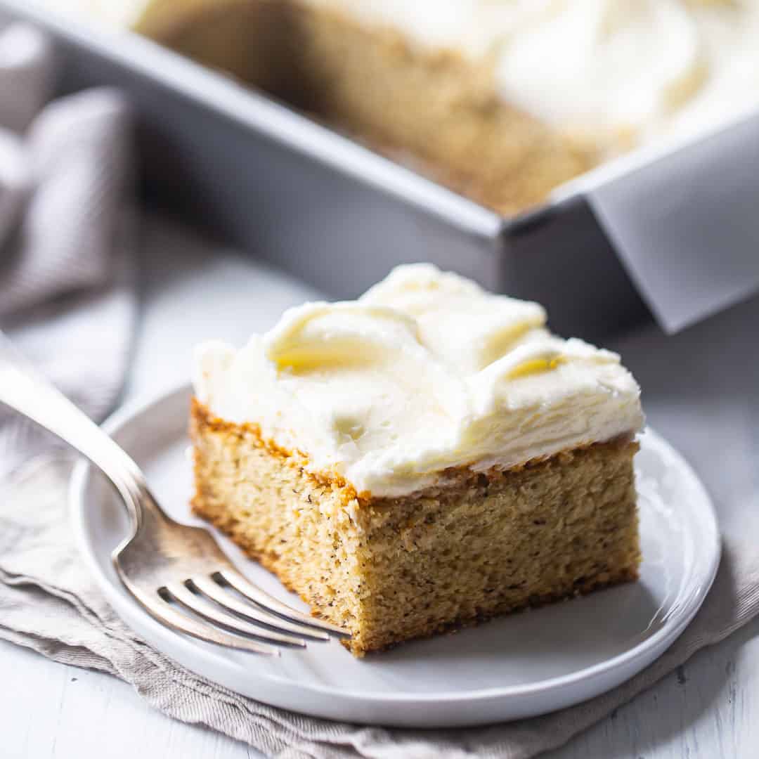 Rebanada cuadrada de pastel de plátano en un plato de porcelana blanca con un tenedor de plata.