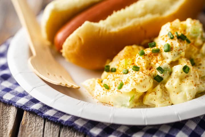 Ensalada de patatas en un plato con una servilleta azul a cuadros y un tenedor desechable.